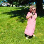 Tessa who is wearing a pink dress is standing on the green at Mt Albert War Memorial Park. She has a microphone in her hand.