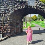 Tessa, mic in hand, stands in front of the memorial arch at Jellicoe Park, Onehunga